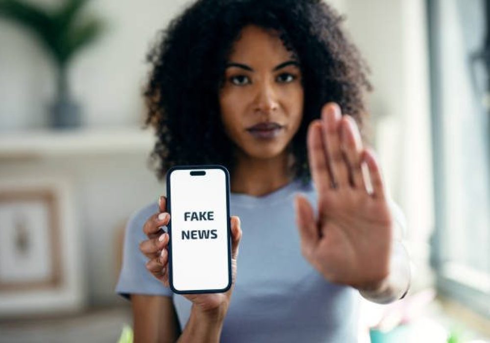 Shot of serious woman holding the mobile phone with the message fake news while doing stop sign with hand at home
